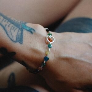 Close-up of a tattooed hand wearing a colorful beaded bracelet with heart shapes.