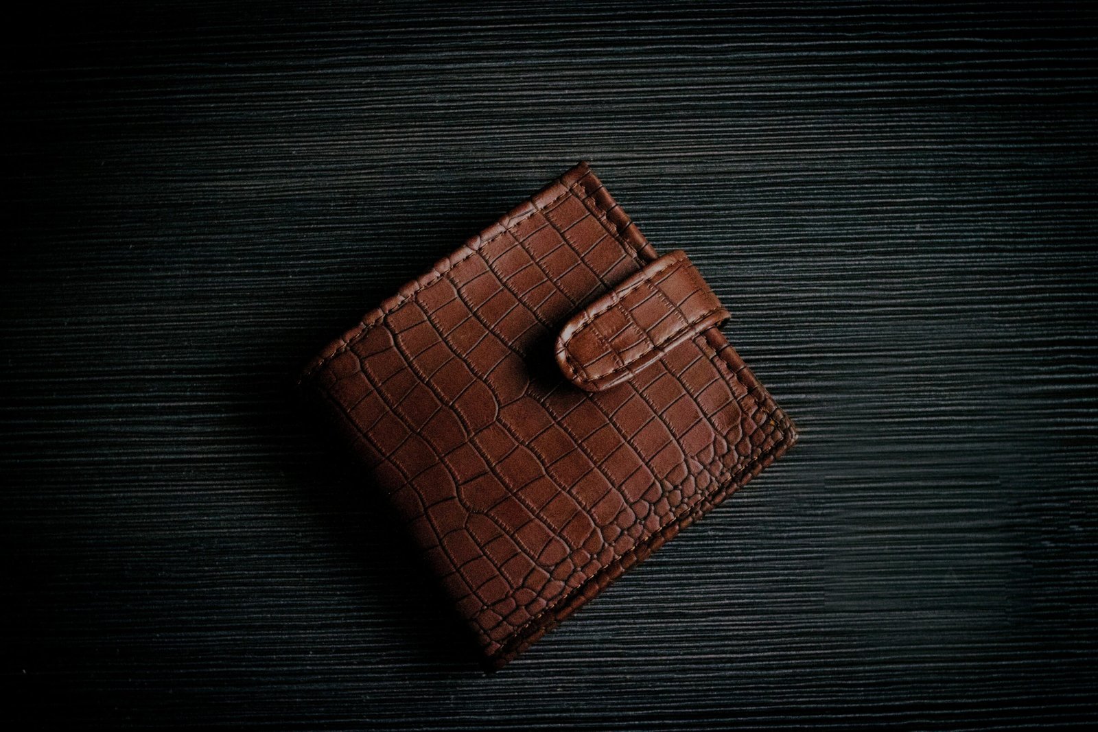 A stylish brown leather wallet with a textured design lies on a dark surface, showcasing its elegant craftsmanship.