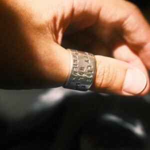 A close-up of a hand wearing an inscribed silver ring, captured in warm sunlight.