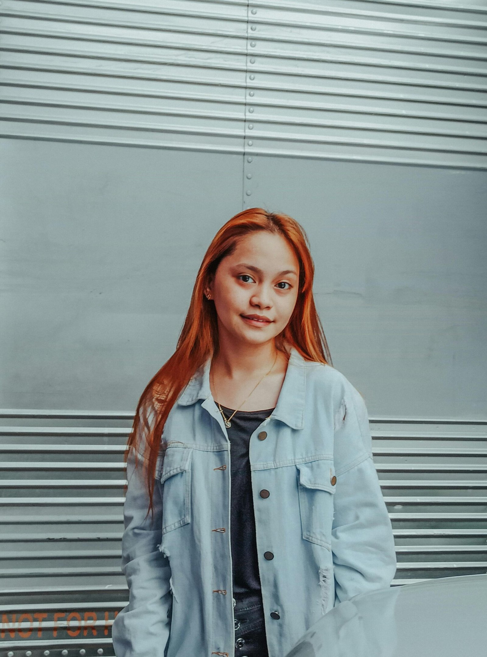 Smiling young ethnic female in casual wear standing against garage wall and looking at camera contentedly