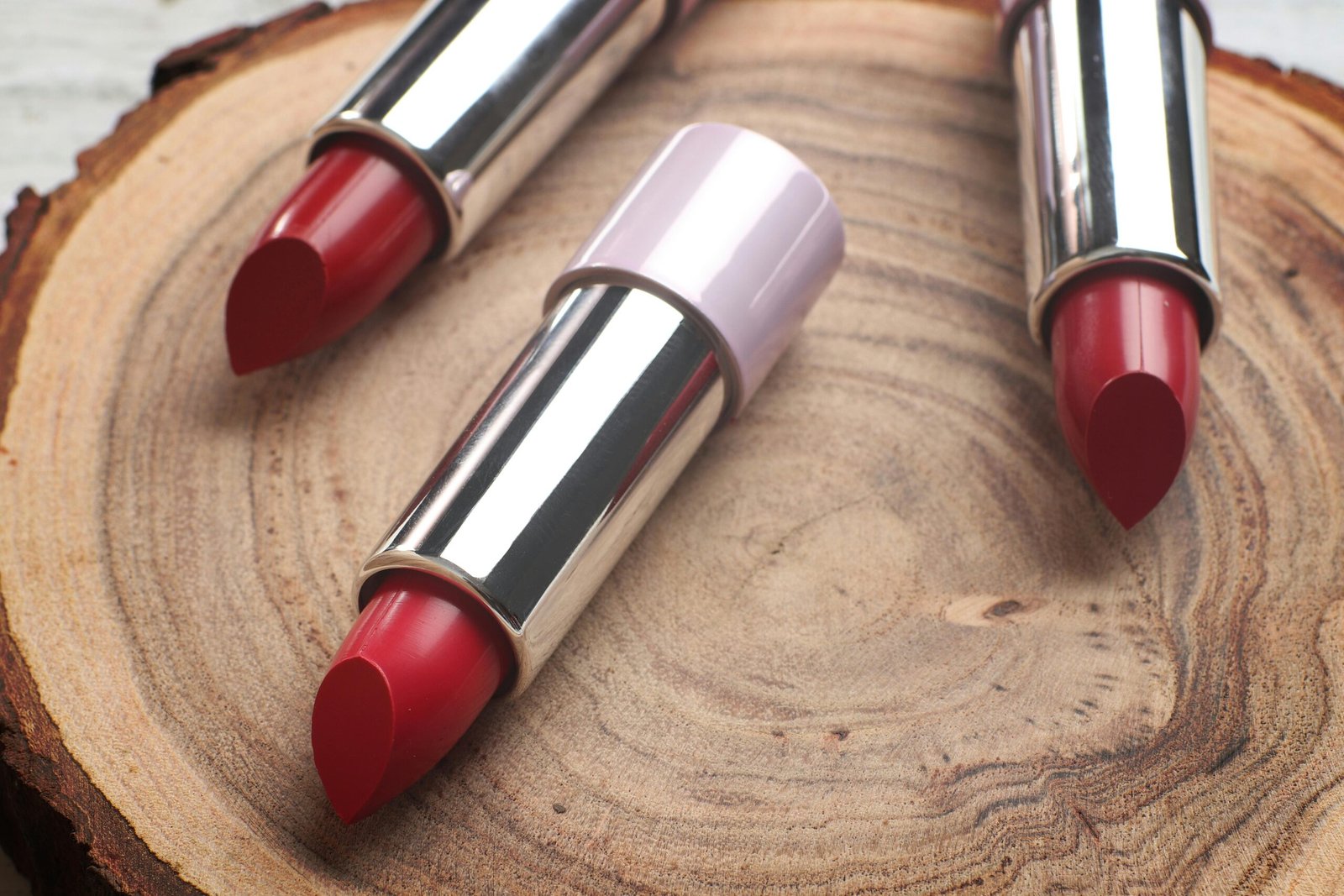 Three red lipsticks arranged on a wooden surface, showcasing vibrant colors and metallic casings.